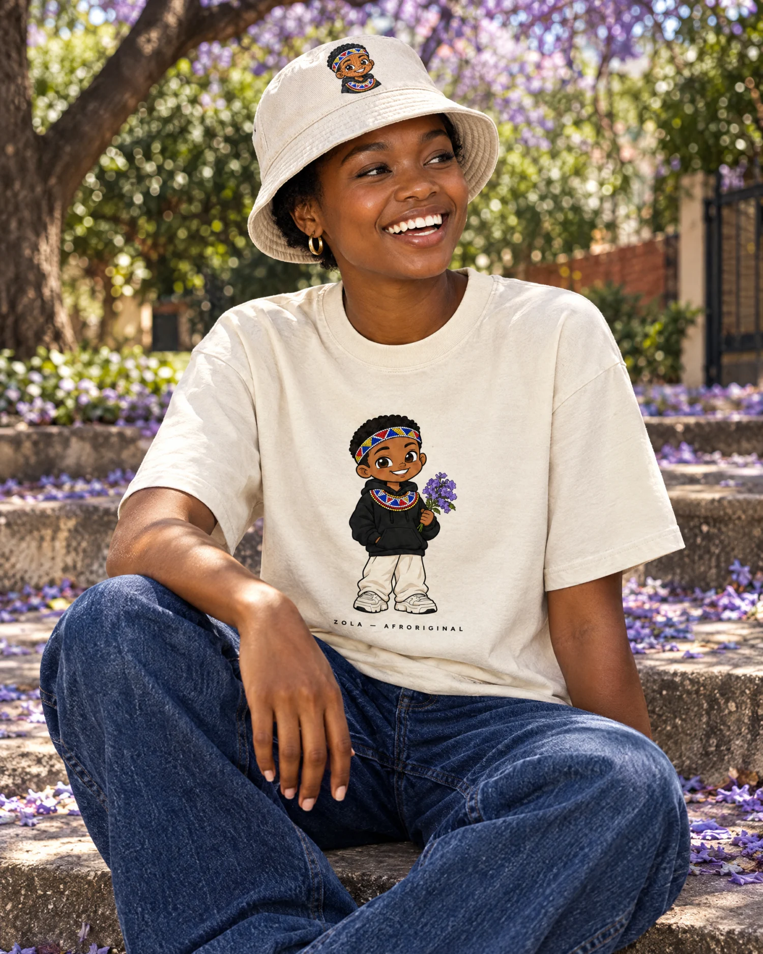 A woman laughs on garden steps covered in jacaranda blossoms wearing the Zola Tee and Zola Bucket Hat
